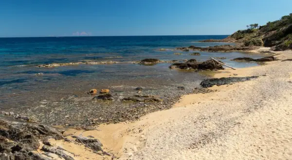 Plage sauvage Narbonne, sable doré, rochers sombres et mer bleue limpide sous un ciel clair. Un coin de paradis préservé.