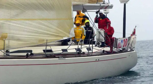 Equipaggio su una barca a vela, con un uomo che sembra D'Alema in giacca gialla.