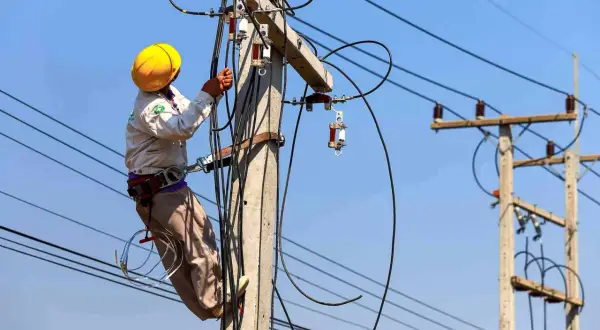 Elektryk w żółtym kasku pracuje na słupie energetycznym, podłączając kable. Zastanawiasz się, ile kosztuje przyłącze prądu?