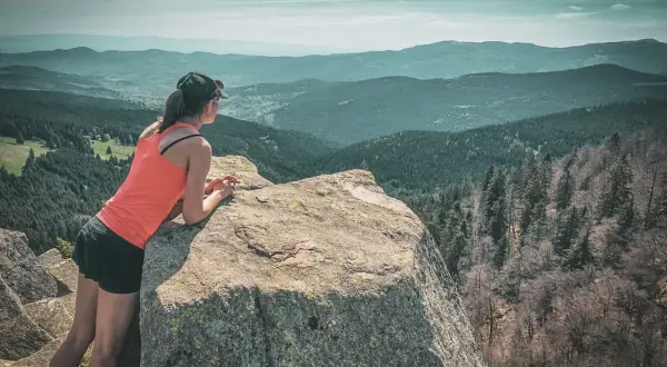 Une femme profite d'une vue panoramique sur les Vosges lors d'un trek. Les montagnes s'étendent à perte de vue sous un ciel nuageux.