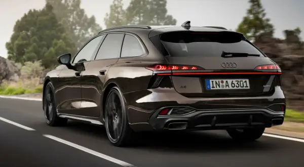 Elegancki Audi Avant w brązowym kolorze jedzie po krętej drodze wśród drzew.