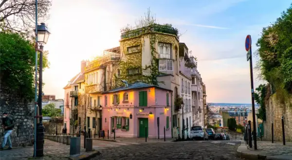 Ein malerisches Viertel in Paris, perfekt für einen Kurztrip. Ein rosa Restaurant mit grünen Fensterläden, umgeben von charmanten Häusern, lädt zum Verweilen ein.