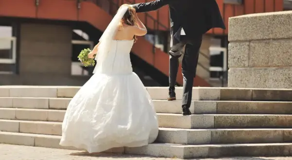 Un couple monte les marches, la mariée en robe blanche tenant un bouquet, le marié en costume noir. Une scène symbolisant leur union, peut-être après une lettre mariage mairie.