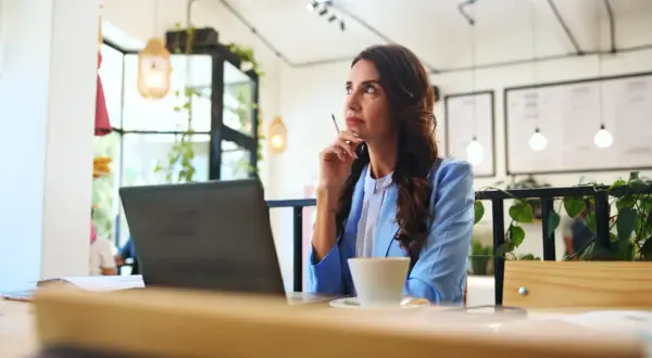Kobieta w niebieskiej marynarce myśli przy kawie, planując swój jednodniowy urlop bezpłatny.