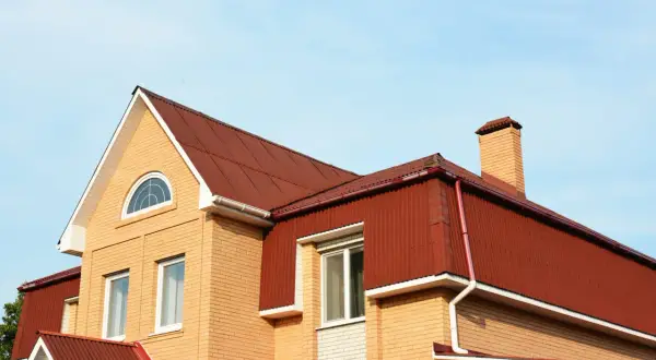 Dom z cegły z czerwonym dachem, okna i komin. Widoczna mansarda, czyli przestrzeń pod dachem.