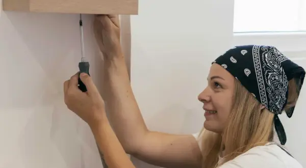 Une femme souriante utilise un tournevis pour fixer deux meubles entre eux sans percer.