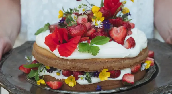 Enkel tårta med vispgrädde, jordgubbar och vilda blommor på ett silverfat.