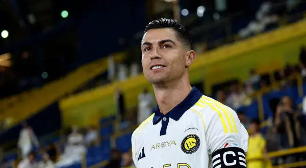 Cristiano Ronaldo w białej koszulce z żółtymi pasami, gotowy do gry. Na ramieniu opaska kapitana.