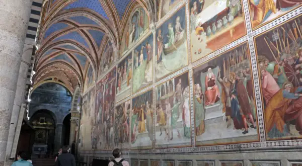 Interno del duomo di San Gimignano con affreschi medievali e volte blu stellate.