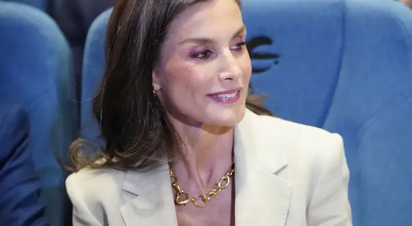 La reina Letizia, con un traje beige y un collar dorado, sonríe mientras asiste a un evento.