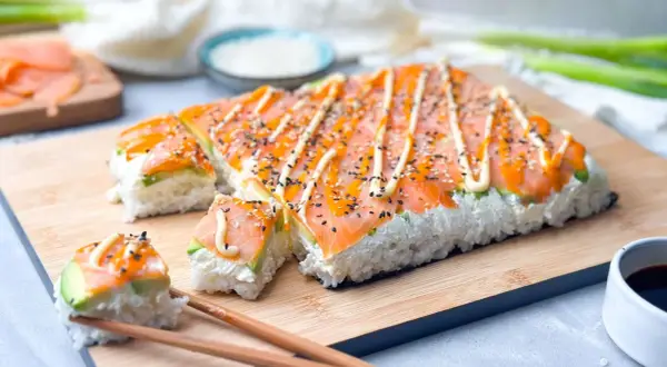 Rechteckige sushi rollen ohne matte, belegt mit Lachs, Avocado und Mayonnaise, bestreut mit Sesam.