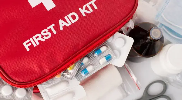 Czerwona apteczka z napisem "FIRST AID KIT", tabletki, bandaże, buteleczka z płynem i maski.