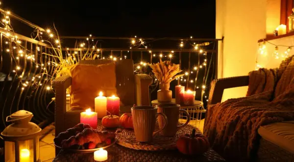Przytulny balkon z jesienne dekoracje diy: migoczące lampki, dynie, świece i gorące napoje.