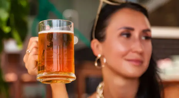 Donna sorridente con in mano un boccale di birra weiss, perfetta per godersi una giornata di sole.