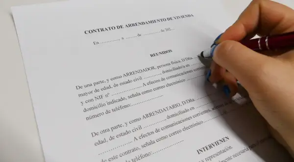 Mano con bolígrafo firmando un contrato de arrendamiento de vivienda. Se detallan los requisitos para alquilar un piso como propietario.