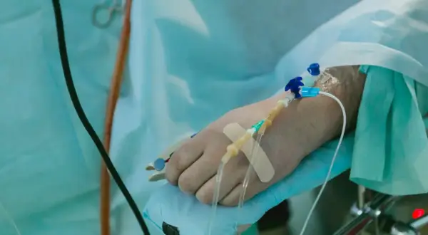 Ręka pacjenta z wenflonem i plastrem, przygotowana do podawania płynów po operacji.