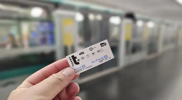 Bilet na metro w Paryżu w dłoni, w tle peron i pociąg.
