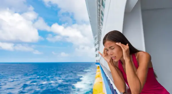 Frau auf Kreuzfahrtschiff mit Kopfschmerzen, fragt sich: Seekrank was tun? Sie lehnt am Geländer, blickt aufs Meer.