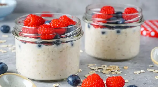 Zwei Gläser mit Overnight Oats, garniert mit Himbeeren und Blaubeeren. Perfekt für gesunde Overnight Oats Rezepte.