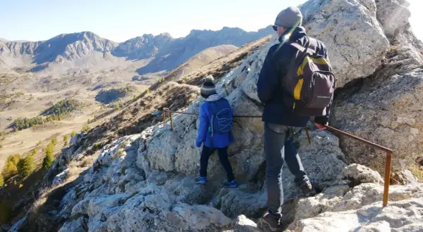 Deux randonneurs escaladent un sentier rocheux dans le cirque de Morgon, avec des montagnes escarpées en arrière-plan.