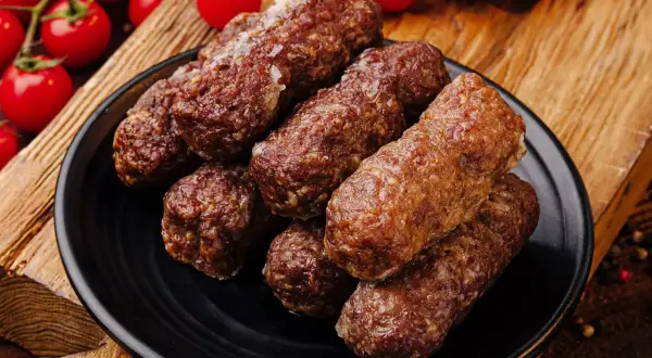 Zrazy z mięsa mielonego, rumiane i soczyste, ułożone na czarnym talerzu, obok gałązek pomidorków koktajlowych.