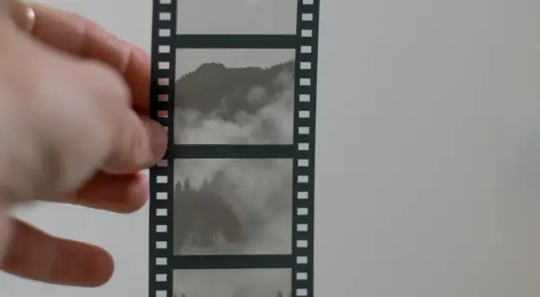Dłoń trzyma kadr z taśmy filmowej, ukazujący mgliste góry i lasy.
