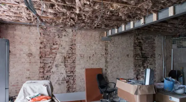 Pågår renovering av funkishus. Synligt bjälklag med isolering och tegelväggar. Material och verktyg ligger utspridda.