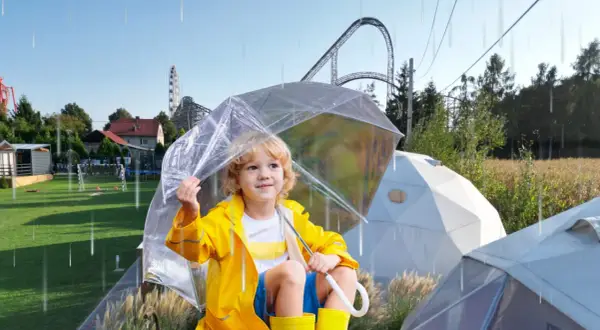 Chłopiec w żółtej kurtce i kaloszach pod przezroczystym parasolem, w tle rollercoaster. Czy Energylandia jest otwarta w deszcz?
