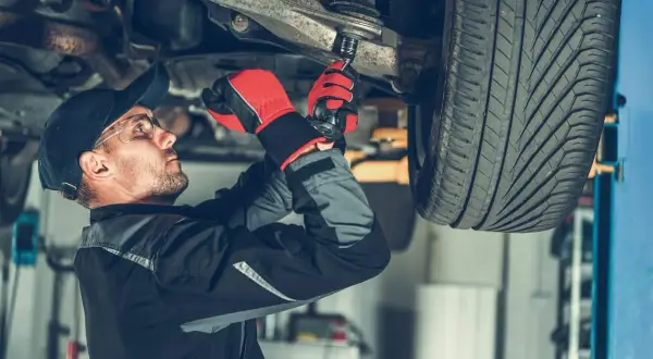 Mechanik dokręca sworzeń w zawieszeniu auta, pracując pod podniesionym pojazdem.