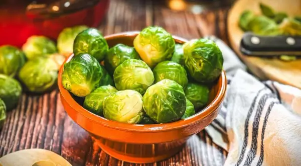 Frischer Rosenkohl in einer Schale, bereit für leckere Rosenkohl Rezepte. Ein Holzlöffel und ein Küchentuch liegen daneben.