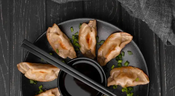 Złociste pierogi z kimchi, posypane szczypiorkiem, czekają na zanurzenie w sosie.