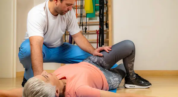 Fizjoterapeuta pomaga pacjentce w wykonaniu testu Patricka, oceniając jej ruchomość stawów biodrowych.