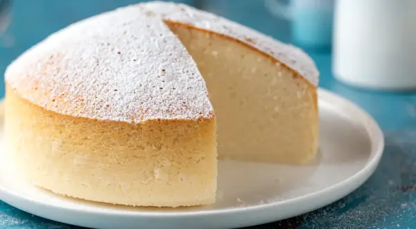 Una soffice torta nuvola, cosparsa di zucchero a velo, attende di essere gustata su un piatto bianco.