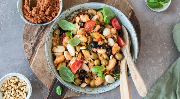 Gnocchi-Salat mit Pesto, Tomaten, Oliven und Pinienkernen in einer Schüssel.