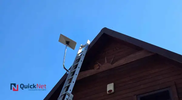 Antena satelitarna Starlink zamontowana na dachu drewnianego domu. Obok drabina, gotowa do pracy.