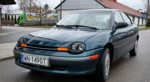 Zielony Dodge Neon z tablicą rejestracyjną WN 1490T stoi na mokrej drodze.