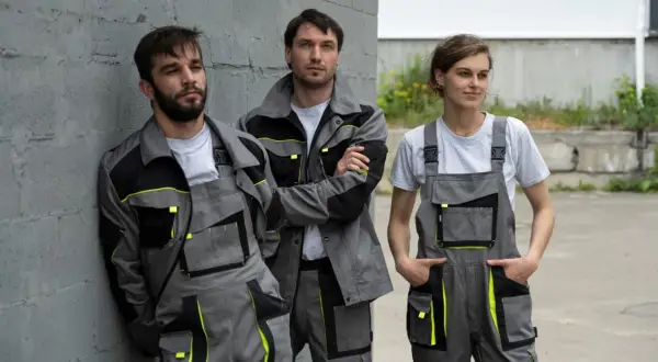 Trzech pracowników w szarych kombinezonach z neonowymi akcentami. Polski producent odzieży roboczej prezentuje nowoczesne ubrania.