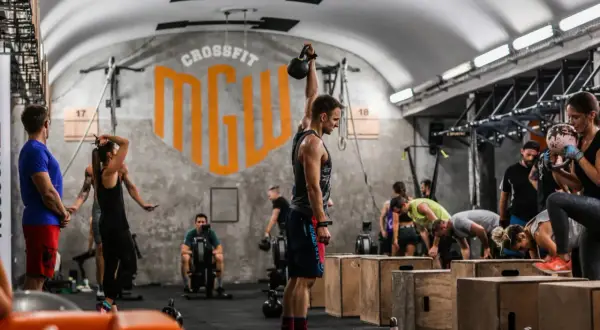 Ludzie ćwiczący CrossFit w siłowni, jeden mężczyzna podnosi kettlebell.