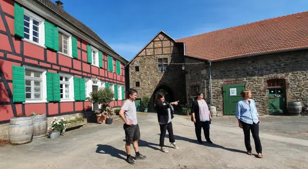 Vier Personen stehen vor einem historischen Fachwerkhaus und einem steinernen Torbogen auf dem Gut Nesselrath.