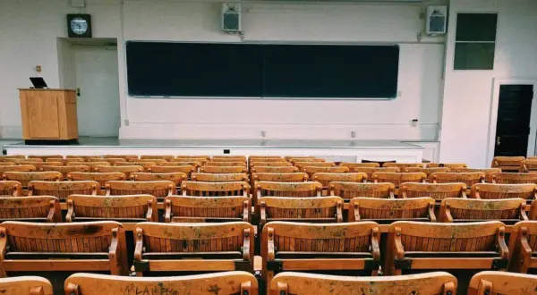 Aula vacía con asientos de madera y pizarra. Un profesor podría hablar aquí, pero para explicar la diferencia entre speak y talk, necesitaría a los estudiantes.