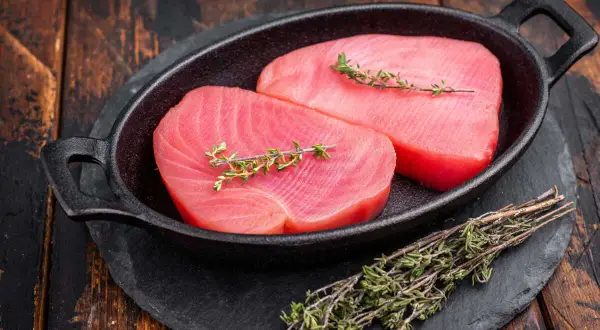 Deux beaux pavés de thon rouge cru, ornés de brins de thym frais, prêts pour une recette savoureuse.