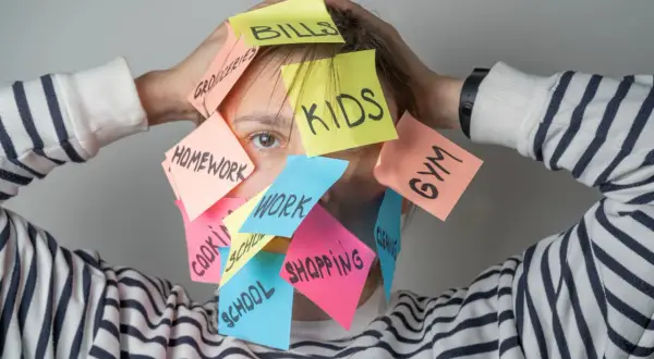 Una persona abrumada por tareas: "Bills", "Kids", "Homework", "Work", "Gym", "Shopping". ¿Cómo ser mejor persona? Prioriza y respira.