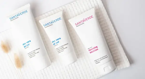 Drei weiße Tuben mit Naturkosmetik, darunter Produkte mit reiner Aloe Vera, liegen auf einem weißen Handtuch.