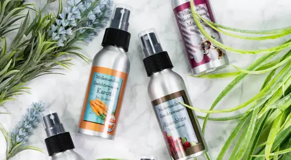 Vier Sprühflaschen mit Gesichtswasser, darunter Karotte und Rosenblüte. Ein Hydrolat ist ein destilliertes Pflanzenwasser, das bei der Herstellung ätherischer Öle anfällt.