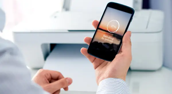 Mężczyzna trzyma smartfon z napisem "Sending to printer", pokazując, jak wydrukować z telefonu przez wifi.