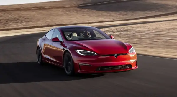 Roter Tesla Model S Plaid fährt auf einer Rennstrecke mit Wüstenlandschaft im Hintergrund.