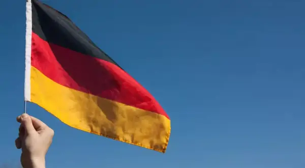 Ręka trzyma flagę Niemiec na tle błękitnego nieba. Chcesz wiedzieć, jak zaadresować list do Niemiec?