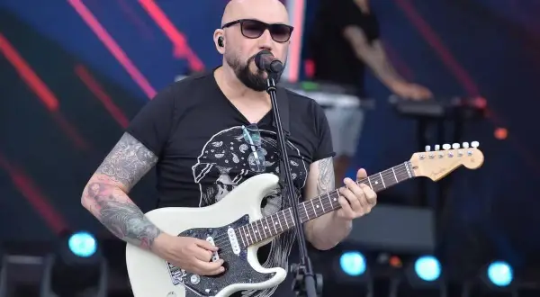 Łysy gitarzysta z tatuażami gra na białej gitarze. W tle klawiszowiec. Koncert, jakby to były kombi piosenki alfabetycznie.