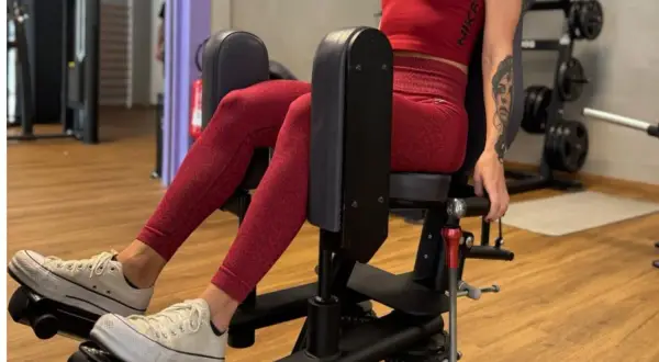 Femme en tenue de sport rouge travaillant son abducteur muscle sur une machine de musculation.
