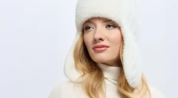 Blondynka w białej, futrzanej czapce uszatce, prezentującej najmodniejsze nakrycia głowy.
